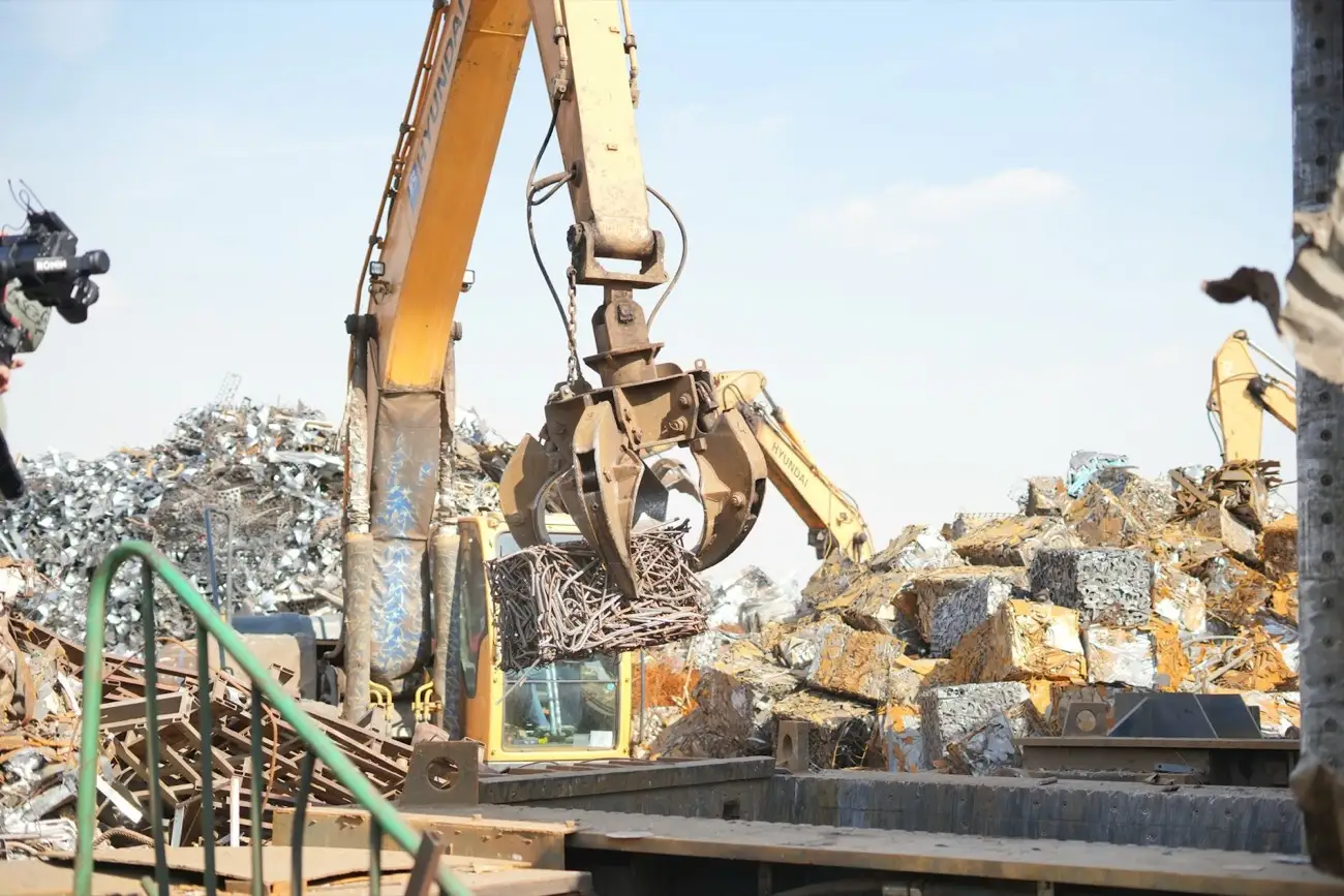 A grapple lifting a bundle of scrap metal beside stacks of baled scrap