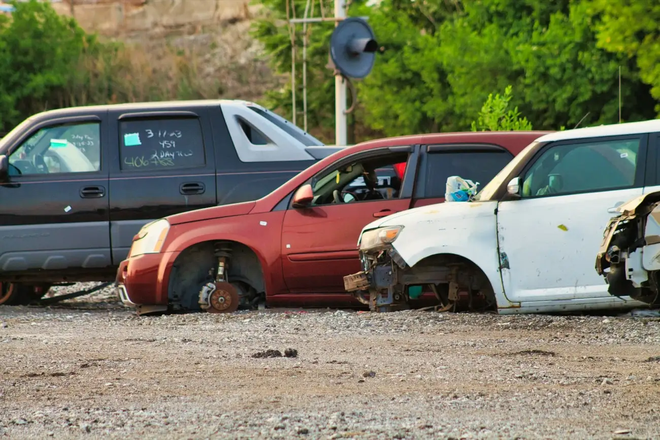 Three stripped cars with missing wheels and panels parked on a gravel lot